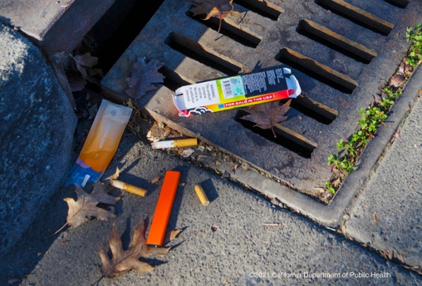 shows a gutter with various vape pens and cigarette butts